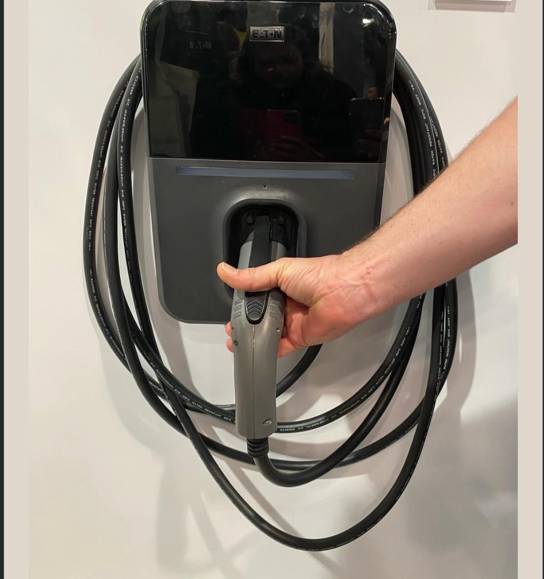 Wall-mounted Level 2 EV charger installed by Sharp Electric, connector in hand
