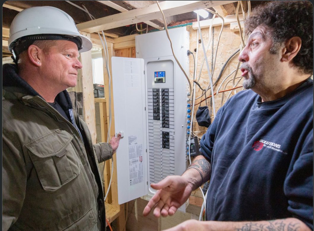 Sharp Electric technician reviewing an open electrical panel with a customer